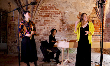 3 Frauen singen und spielen Musik vor einem kaputten Wand