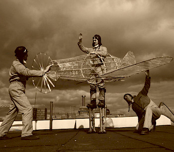 Grau-Bild: 3 Männer versuchen 1 Modell des Flugzeuges zu starten