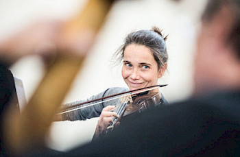 Tabea Höfer spielt Geige. Das Photo wurde über die Schulter von Christian Raudszus fotografiert, der im Vordergrund noch leicht verschwommen zu erkennen ist.